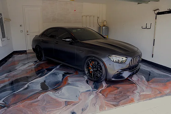 A dark grey sedan parked on the same copper and white metallic floor, its wheels reflected in the gloss