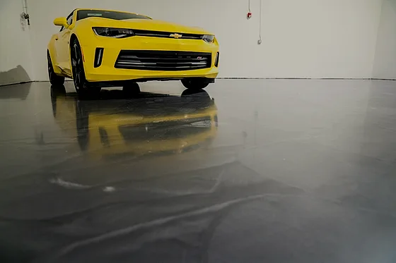 A pewter metallic floor with soft cloud veining filling a garage bay, a yellow car standing on it and mirrored in the surface