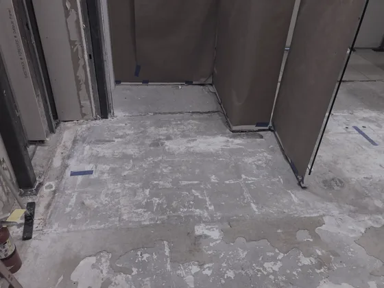 A stripped retail slab before coating, old adhesive ghosting across it, blue layout tape and kraft-wrapped fixtures at the edges