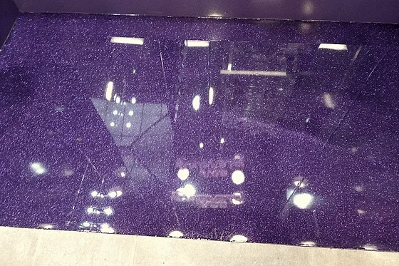 A deep purple glitter epoxy floor running up to a painted wall, its flake and the store's ceiling lights reading back off the finished surface