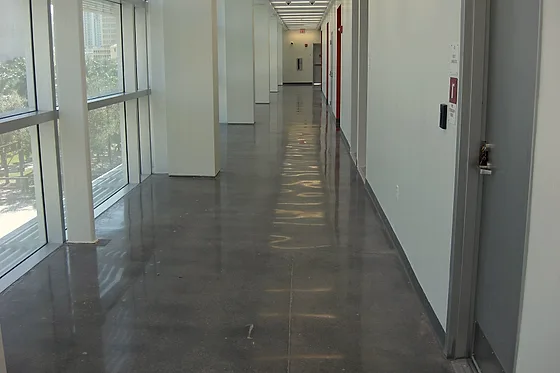 A glazed corridor over grey polished concrete, daylight reflecting the full length of the floor