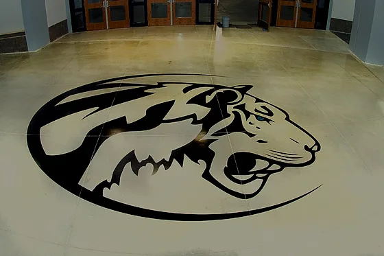 A large animal figure ground and stained into a polished lobby floor, set inside the saw-cut joint grid in front of the entrance doors